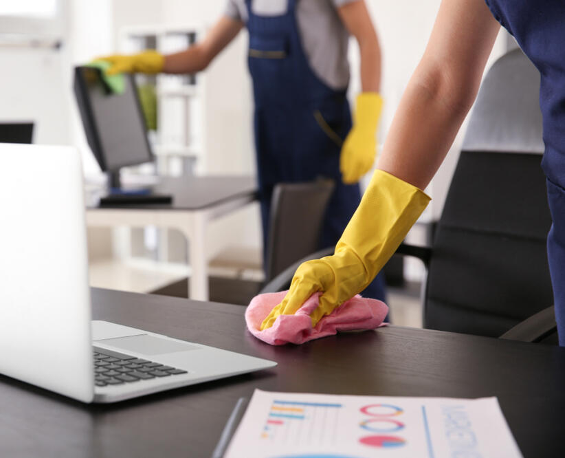 Professional Office Cleaning Services wo professional cleaners sanitizing an office workspace with gloves and cloths.